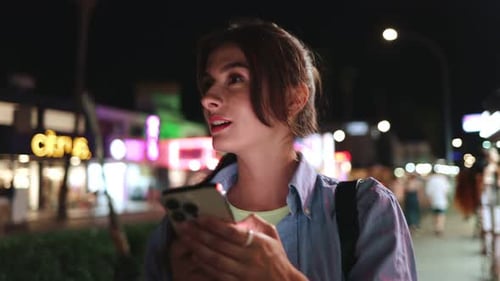 Portrait View of Happy Stunning Young Woman Walking at Streets of Night City Holding and Looking at