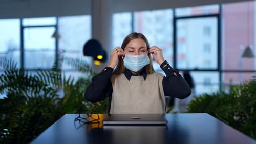 Woman Puts on Surgical Mask in Modern Office