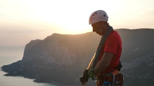 A Climber with Equipment in His Hands Stands on Top of a Mountain Overlooking the Sea