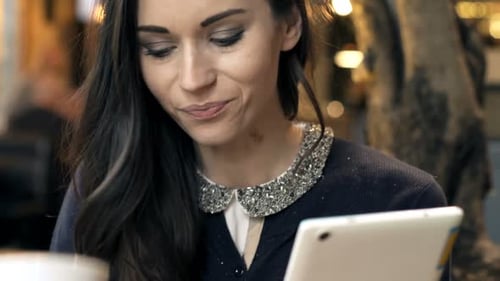 Happy Woman Reading Book on Tablet and Drinking Coffee in Cafe 30s