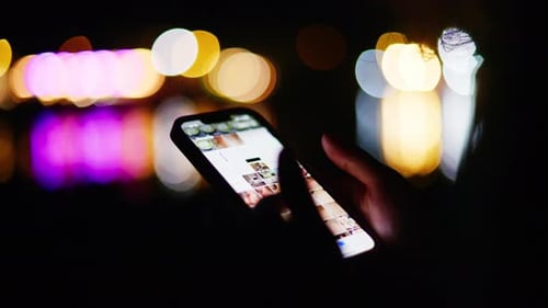 Woman scrolling on her phone on the beach at night