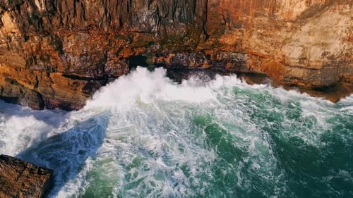 Powerful sea waves crashing on rocky coastline cliffs on a sunny day