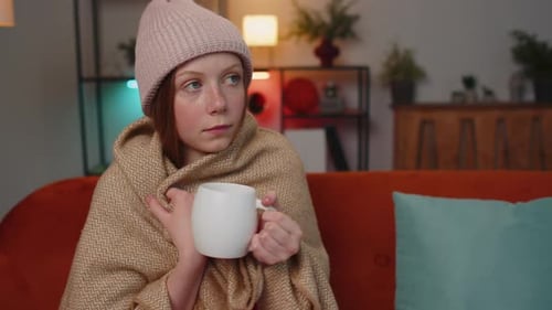 Sick Children Girl Wear Hat Wrapped in Plaid Sit Alone Shivering From Cold on Sofa Drinking Hot Tea