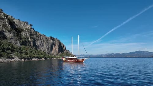 Serene Coastal Sailboat Scene: A classic sailboat gracefully navigates tranquil waters, framed by lu