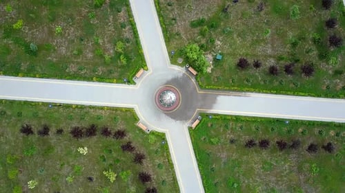 Paths in the park with fountain in the middle and four benches.
