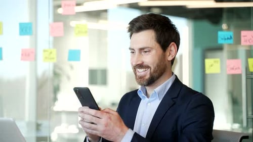 Professional businessman in modern office uses smartphone for work related tasks.