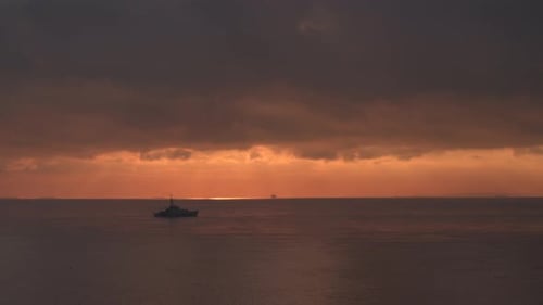 Wide aerial view of a Royal Navy Warship sailing on a calm sea at sunrise.