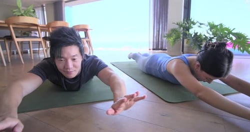 Pareja asiática en ropa deportiva bajando la cabeza plantando las manos presionando contra la cobra para hacer ejercicio en casa