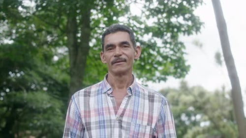 Smiling Man in Plaid Shirt Stands Outdoors
