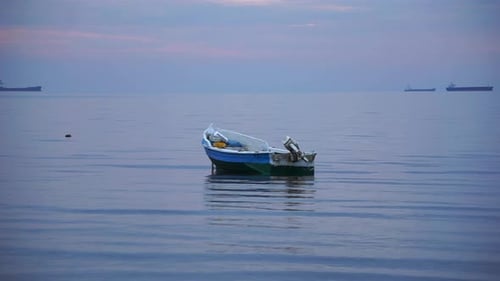 Lonely boat on still water with ships on the distant horizon
