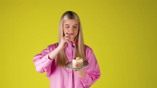 Young Blonde Woman Holding Plate Of Cake and Eating With Fork, Studio Portrait