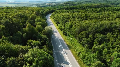 Footage over the highway with few cars riding by. Green countryside in summer.