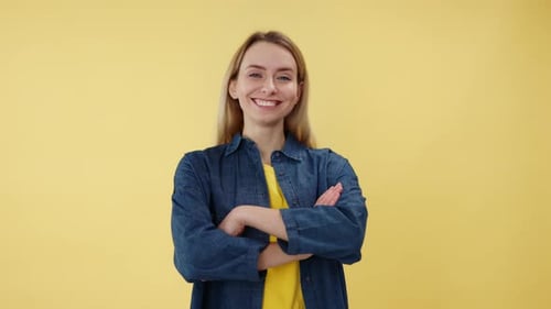 Woman Crossing Arms and Smiling While Looking at Camera Over Yellow Background
