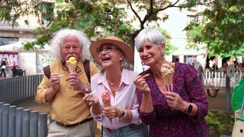 Three Cheerful Senior Friends Tasting Gelato Together in an Urban Park
