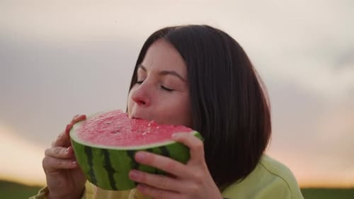 Woman Bites Delicious Watermelon at Sunset in Field