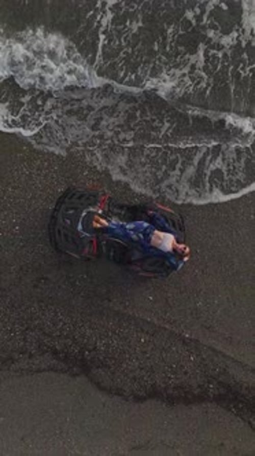 Vertical Video ATV and Model Posing on the Beach With Rolling Ocean Waves Behind Them