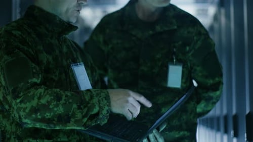 In Data Center Two Military Men Work with Open Server Rack Cabinet. One Holds Military Edition Lapt