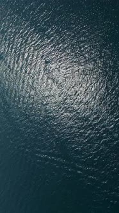 Luftaufnahme der dunkelblauen Meeresoberfläche mit funkelnden Sonnenlichtreflexen und sanften natürlichen Wellen