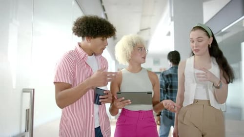 Collaborating on project details, colleagues using tablet in modern office hallway