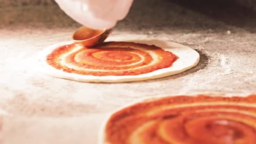 Koch bereitet Pizzateig mit Tomatensauce für den Ofen bei hellem Licht in der Küche vor