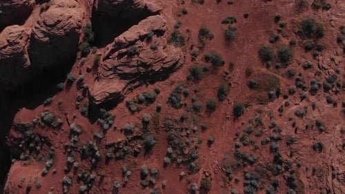 Drone looking down, then slowly panning up while flying forward over red rock, looking at city.
