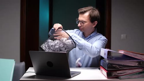 Office Worker Emptying Wastebasket Full of Crumpled Paper Into Laptop