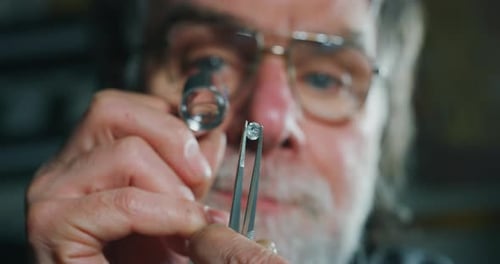 Slow motion close up of experienced goldsmith controlling a quality of diamond stone, selected for