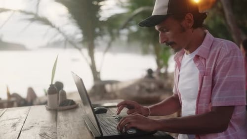 Software Developer Works on Laptop at Beach Cafe Sunset Light on Ocean Man in Casual Outfit Codes