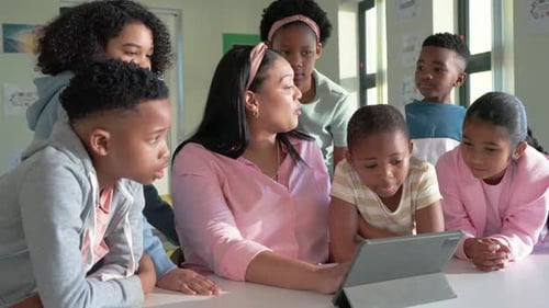 Mentor woman, pink blouse, headband holding tablet drawing students, pointing, teaching at school