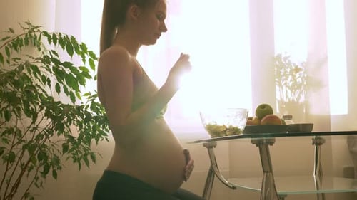 Pregnant Woman Eats Salad at Home in Sunlight