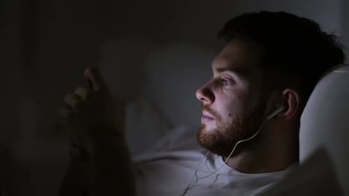Young Man Using Cellphone in Bed at Night