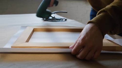 Hands Stretching Canvas onto Wooden Frame in Studio
