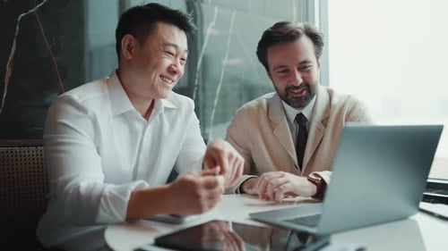 Dos colegas multinacionales sonrientes hablando sobre el trabajo mientras están sentados en la oficina