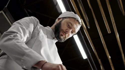View From Below on Caucasian Handsome Male Baker in Apron and Hat Working and Making Bread or Pastry