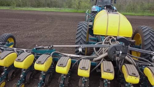 Blue tractor with yellow seeder working on the field in Ukraine OA