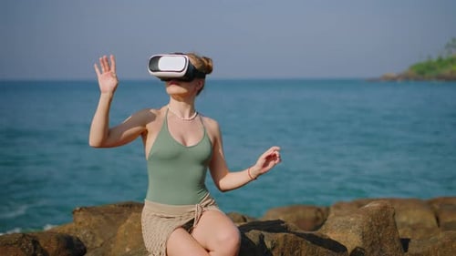 Woman in VR Headset Explores Digital World Seated on Coastal Rocks Virtual Reality Experience By Sea