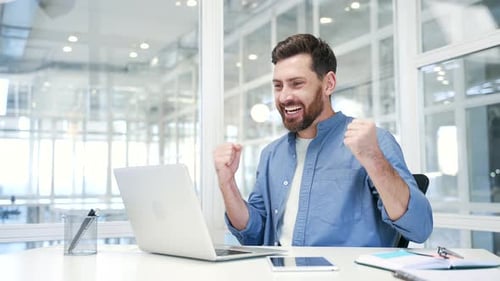 Man Cheers at Desk After Laptop Success