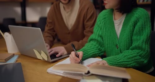 Close Up a Brunette Girl and a Guy are Sitting at a Table Near a Laptop and Books in the Library