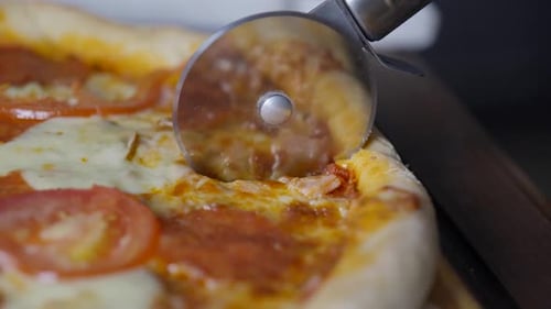 Slicing a hot pizza pie. Close-up tracking shot following the pizza cutter.