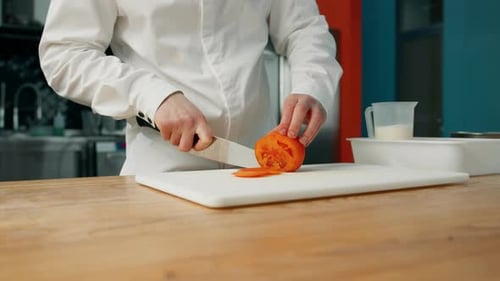 professional kitchen: the chef slowly cuts a tomato to prepare a burger or salad.