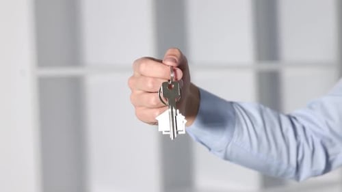 Real estate agent holding key with house shaped keychain indoors, closeup