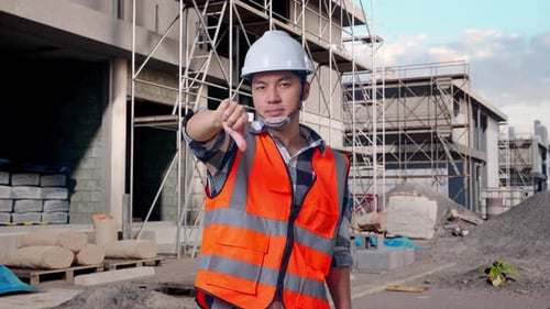 Asian Male Engineer Showing Thumbs Down Gesture And Shaking His Head At Building Site