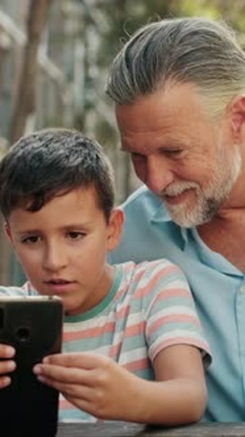 Child and Adult Looking at Phone Together Outdoors