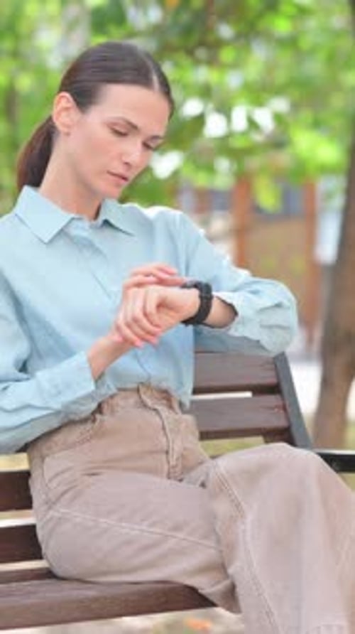 Woman Checks Smartwatch While Sitting On Park Bench