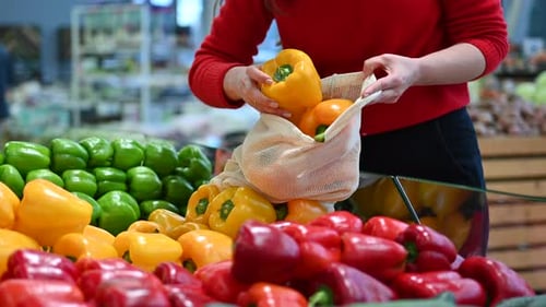 Mujer recogiendo pimientos en una bolsa reutilizable en una tienda. Temáticas del Día de la Tierra y la Ecología. Cámara lenta