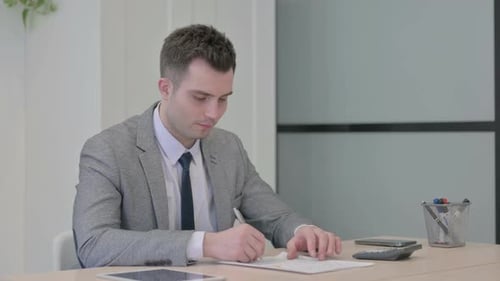 Young Adult Reviews Paperwork in Bright Office
