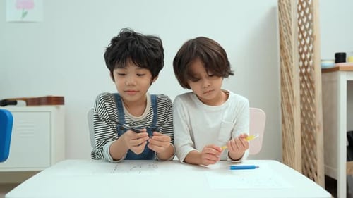 Happy asian two boy kids creatively draw and talk with brushes and crayon on the table.