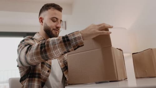 Young Adult Opens a Cardboard Box and Smiles