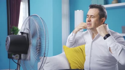 Man trying to cool off with fan at home.