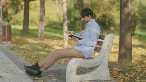 Junger Mann entspannt sich mit einem Buch auf einer Parkbank in einer ruhigen Herbstkulisse
